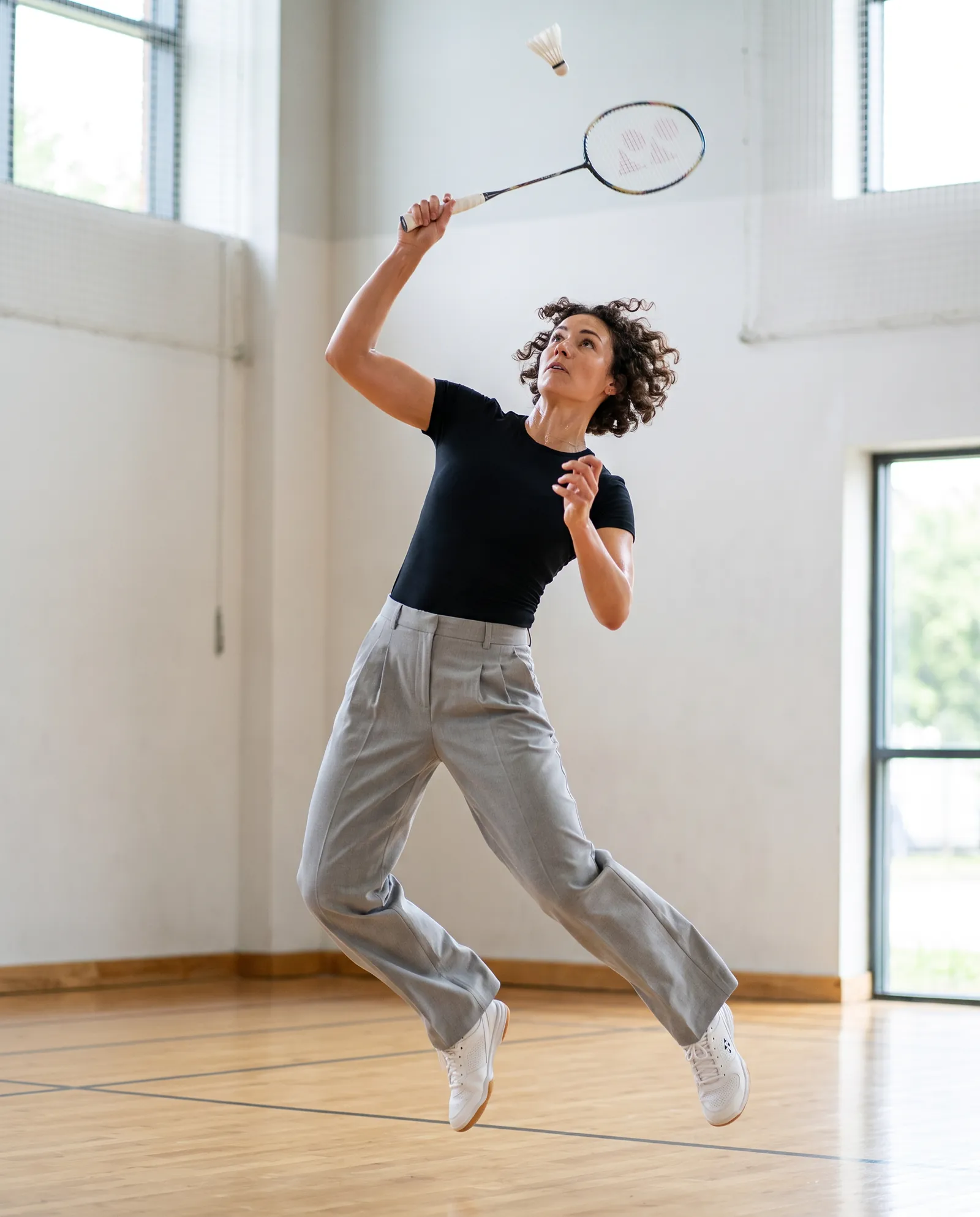 The same pleated trousers mid-jump during an overhead badminton smash